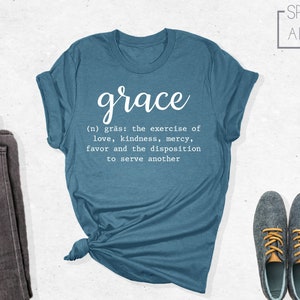 Op de afbeelding: Een tealblauw t-shirt met het woord "grace" in witte, cursieve letters. De definitie van genade staat eronder in witte letters: "(n) gr&auml;s: de uitoefening van liefde, vriendelijkheid, barmhartigheid, gunst en de bereidheid om een ander te dienen".