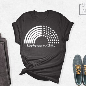 May include: A dark gray t-shirt with a white rainbow and hearts design. The text "kindness matters" is printed below the rainbow.