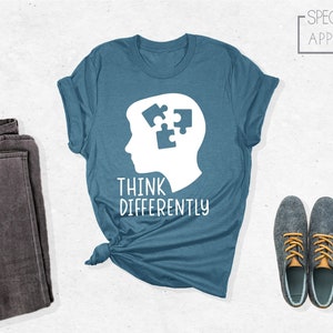 May include: A blue t-shirt with a white silhouette of a head with puzzle pieces inside. The text "Think Differently" is printed below the head.