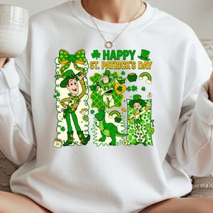 A woman wearing a white sweater with a graphic design of St. Patrick's Day characters and text, holding a mug and making a peace sign.