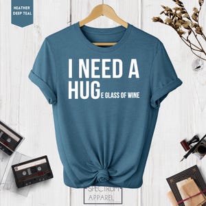 May include: A blue t-shirt with the text "I need a hug and a glass of wine" printed in white.