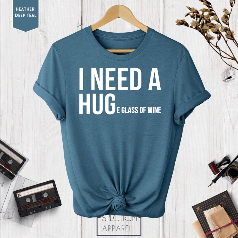 May include: A blue t-shirt with the text "I need a hug and a glass of wine" printed in white.
