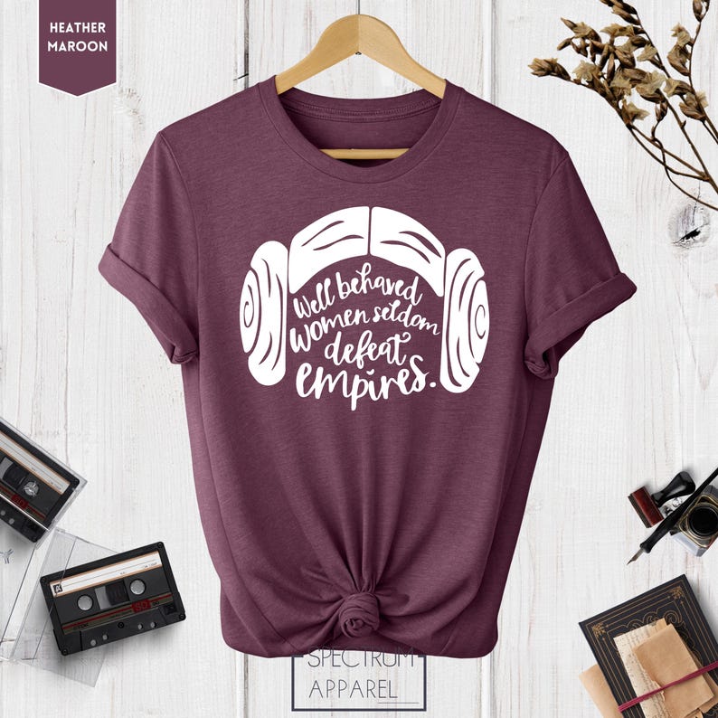 Puede incluir: Una camiseta de color marr&oacute;n jaspeado con un gr&aacute;fico blanco de los mo&ntilde;os de la princesa Leia y el texto "Well behaved women seldom defeat empires."