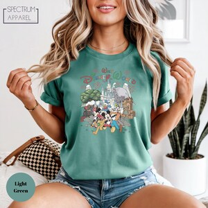 A woman wearing a green t-shirt with a Disney World graphic and shorts is posing for a photo.