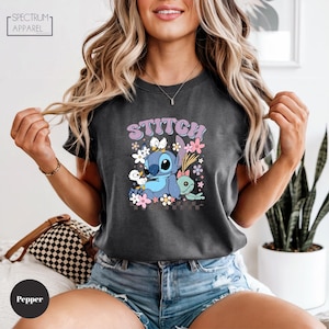 A woman wearing a black t-shirt with a graphic of Stitch and flowers, smiling and posing with her hands in the air.