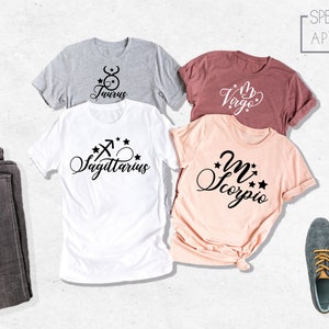 May include: Four t-shirts with different zodiac signs printed on them. The signs are Taurus, Virgo, Sagittarius, and Scorpio. The shirts are laid out on a white surface. The text "SPECTRUM APPAREL" is printed on a white rectangle in the upper right corner of the image.