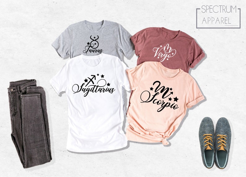 May include: Four t-shirts with different zodiac signs printed on them. The signs are Taurus, Virgo, Sagittarius, and Scorpio. The shirts are laid out on a white surface. The text "SPECTRUM APPAREL" is printed on a white rectangle in the upper right corner of the image.