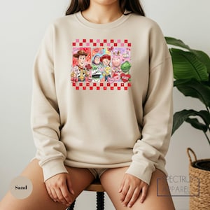 A person wearing a beige sweatshirt with a colorful graphic of characters from the Toy Story movie.