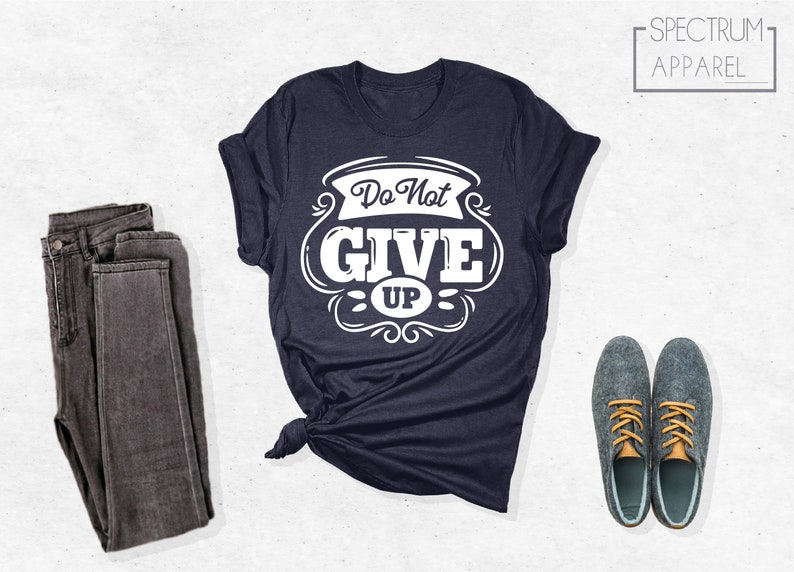 May include: A navy blue t-shirt with a white graphic that says "Do Not Give Up" in a vintage style font. The shirt is folded and laid flat on a white surface.