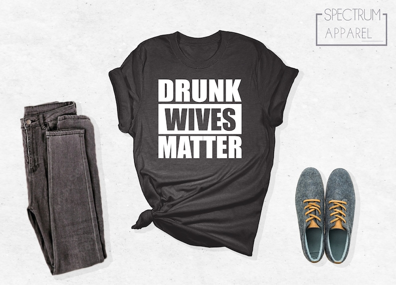 May include: A dark gray t-shirt with the text "DRUNK WIVES MATTER" printed in white.