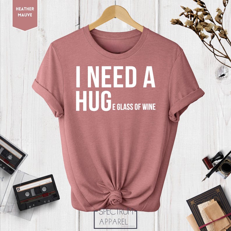 May include: A heather mauve t-shirt with the text "I need a hug and a glass of wine" printed in white.