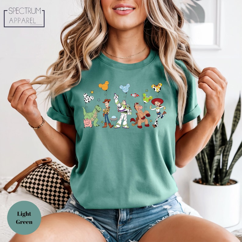 A woman wearing a green t-shirt with a graphic of characters from the Toy Story franchise, including Woody, Buzz Lightyear, and other beloved characters.