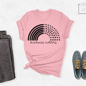 May include: Pink t-shirt with a black rainbow and hearts design. The text "kindness matters" is printed below the rainbow.