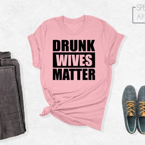 May include: Pink t-shirt with black text that reads "Drunk Wives Matter".