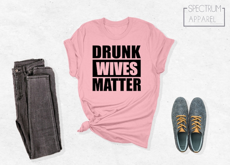 May include: Pink t-shirt with black text that reads "Drunk Wives Matter".
