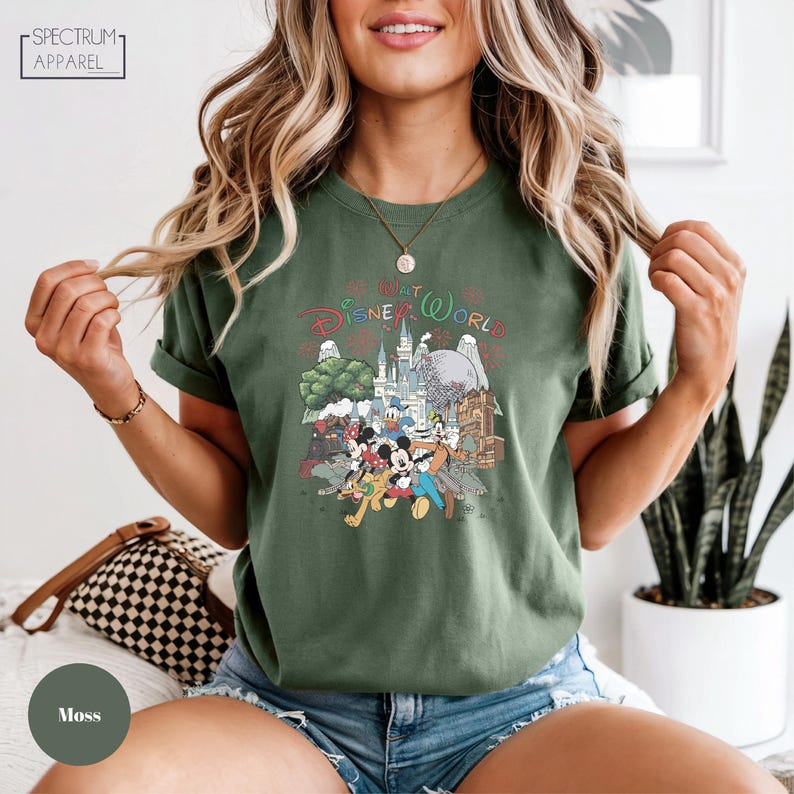 A woman wearing a green t-shirt with a Disney World graphic and a necklace is posing for the camera.