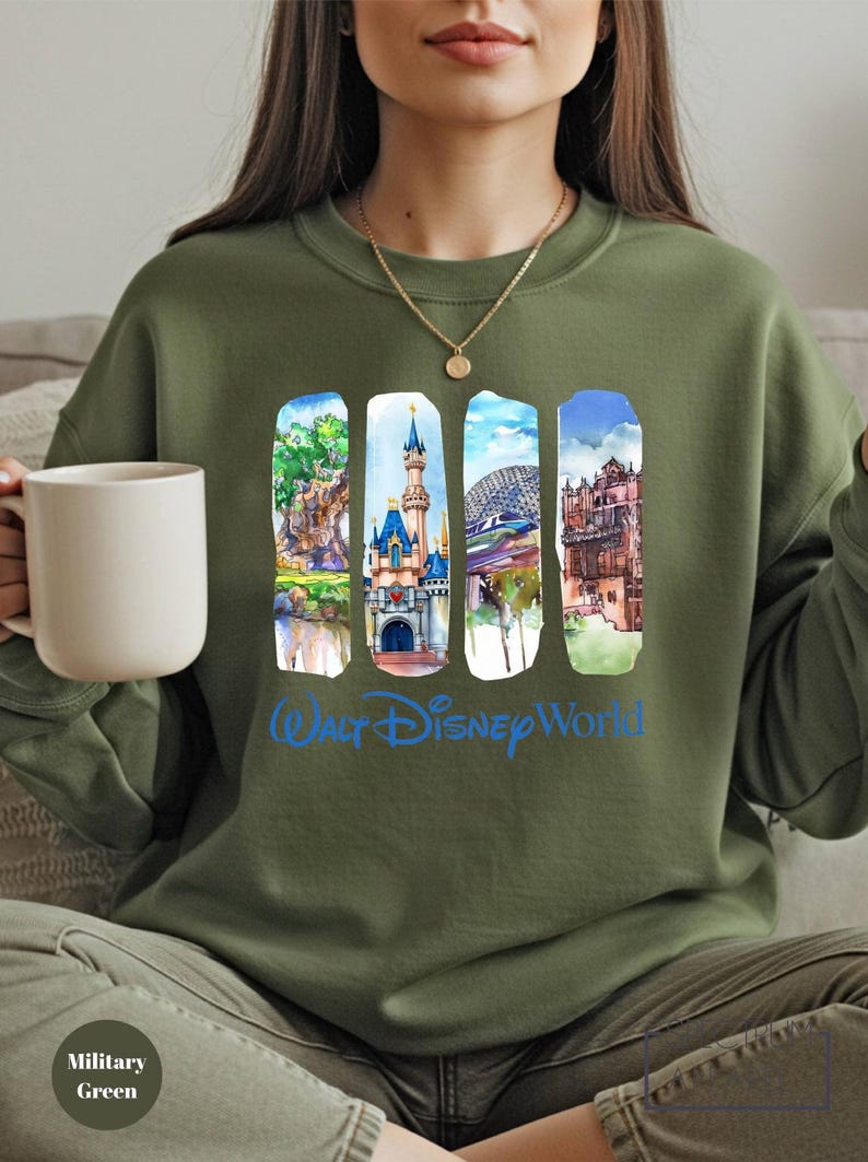 A woman wearing a green sweatshirt with a collage of Disney World images on it, holding a white mug.