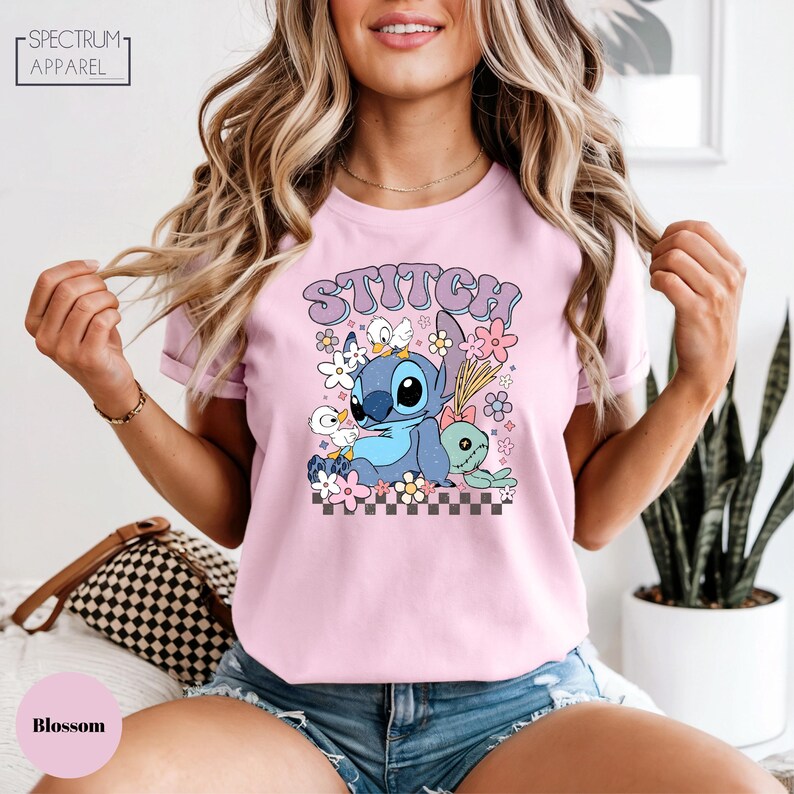 A woman wearing a pink t-shirt with a cartoon character and floral design, smiling and posing.