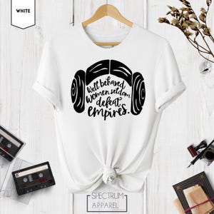 Puede incluir: Camiseta blanca con un gr&aacute;fico negro de la cabeza de una mujer con un mo&ntilde;o lateral y el texto "Well behaved women seldom defeat empires."