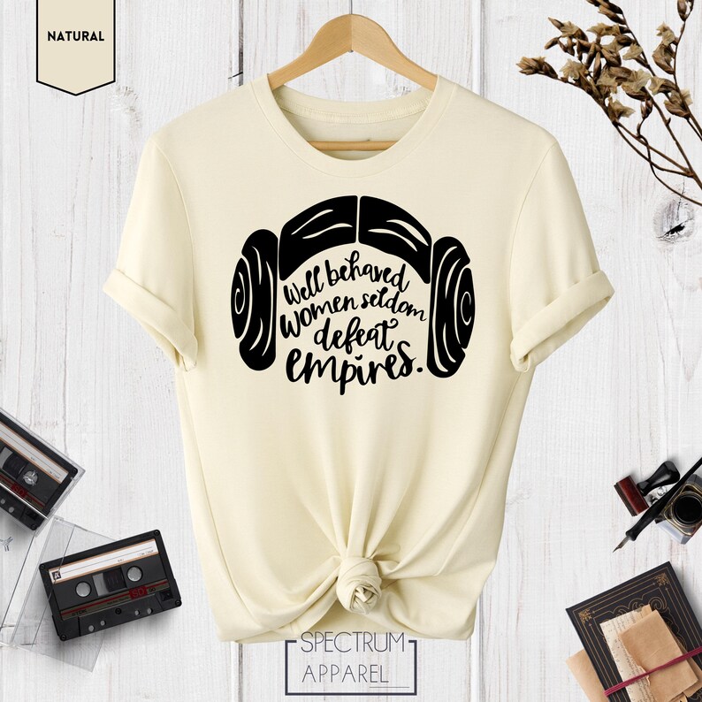 Puede incluir: Una camiseta de color crema con un gr&aacute;fico negro de los mo&ntilde;os de pelo de la princesa Leia y el texto "Well behaved women seldom defeat empires."