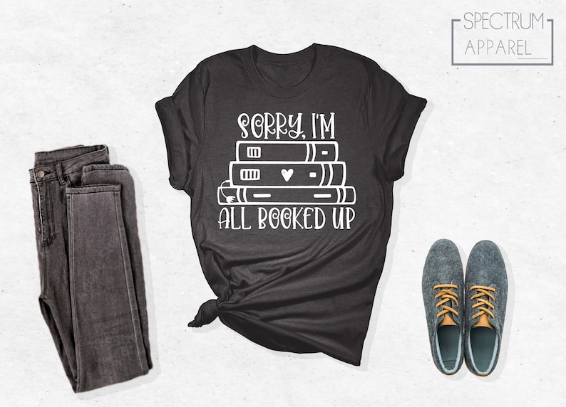 May include: A dark gray t-shirt with the text "Sorry, I'm all booked up" and a stack of books with a heart on the top book.