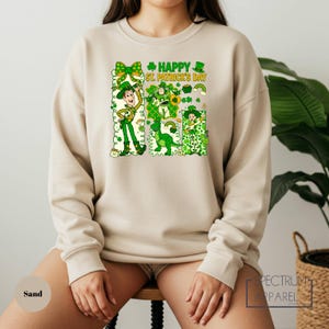 A woman wearing a beige sweater with a graphic design featuring cartoon characters and text related to St. Patrick's Day.