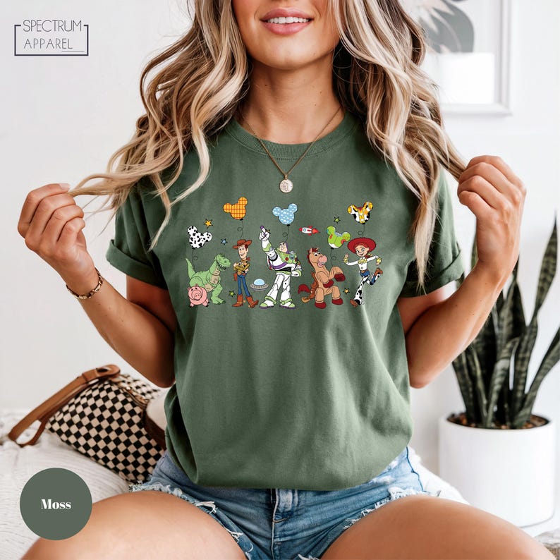 A woman wearing a green t-shirt with a graphic of various cartoon characters, including a dog, a cat, and other popular characters from the Toy Story franchise.