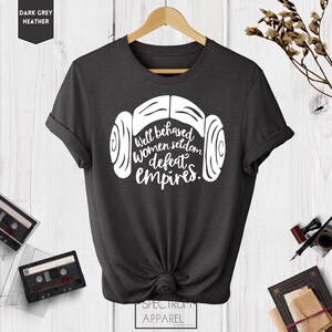 Puede incluir: Camiseta de color gris oscuro jaspeado con un gr&aacute;fico blanco de un casco de un personaje de Star Wars y el texto "Well behaved women seldom defeat empires."
