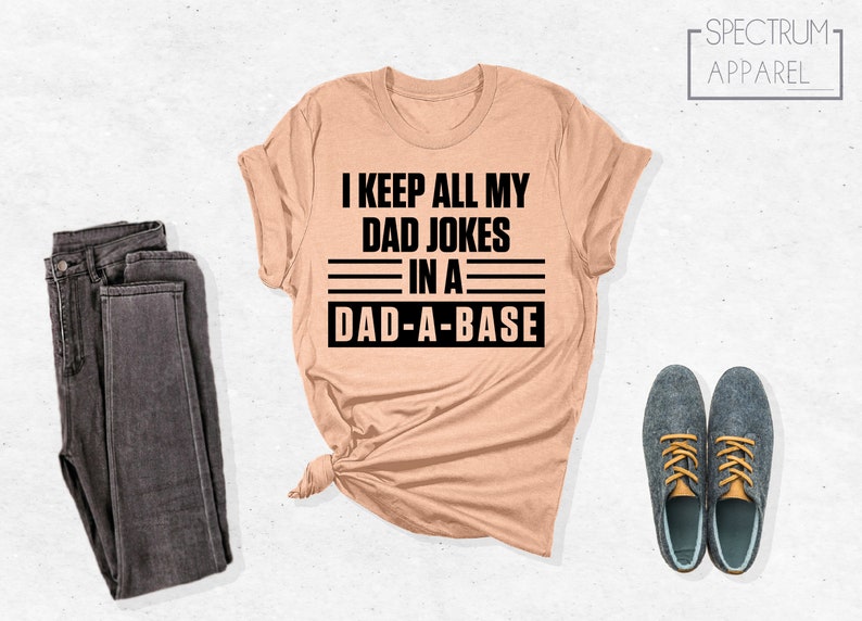 May include: A peach-colored t-shirt with black text that reads "I keep all my dad jokes in a dad-a-base".