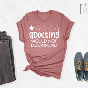 May include: A pink t-shirt with a white graphic that says "Adulting would not recommend" and has five white stars above the text.