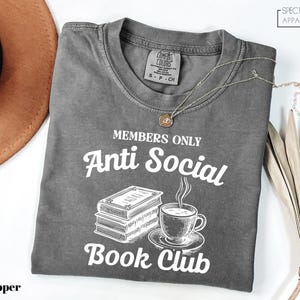 a gray t-shirt with a graphic design that reads "MEMBERS ONLY Anti Social Book Club" and includes a book and a cup of coffee.