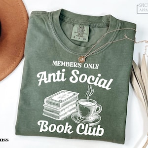 a green t-shirt with white text and graphics, including a book and a cup of coffee, along with a necklace and a hat.