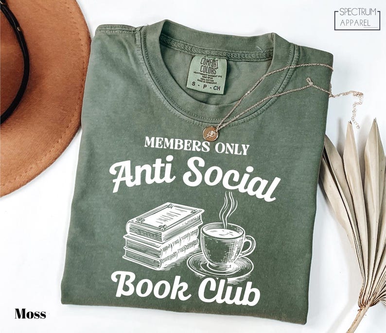 a green t-shirt with white text and graphics, including a book and a cup of coffee, along with a necklace and a hat.