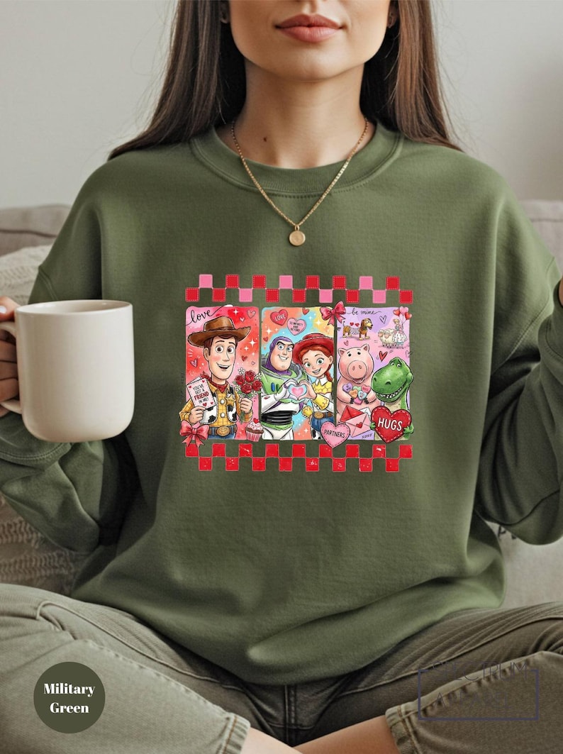 A woman wearing a green sweatshirt with a graphic of characters from the Toy Story movie, including Woody, Buzz Lightyear, and Piggy, holding a white mug.