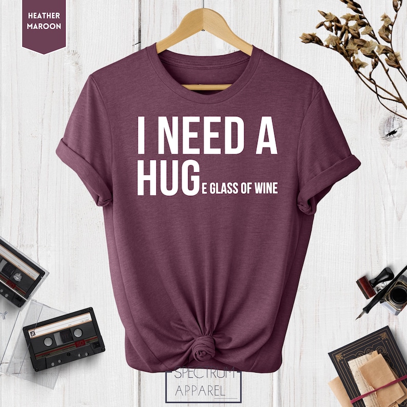 May include: A heather maroon t-shirt with the text "I need a hug and a glass of wine" printed in white.