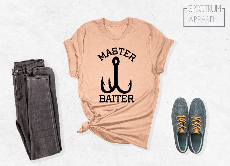 Pode incluir: Uma camiseta cor de p&ecirc;ssego com um gr&aacute;fico preto de um anzol de pesca e o texto "Master Baiter".