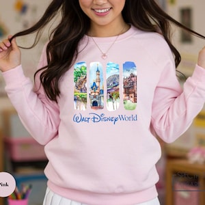 A woman wearing a pink sweatshirt with a collage of Disney World images on it.
