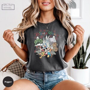 A woman wearing a black t-shirt with a Disney World graphic and denim shorts, smiling and posing with her hands in the air.
