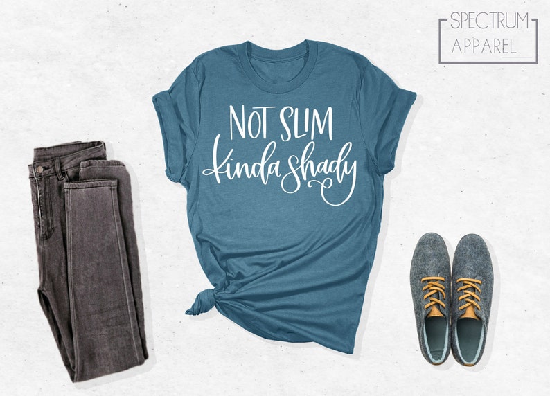 May include: A blue t-shirt with the text "Not Slim Kinda Shady" in white lettering. The shirt is folded and laid flat on a white surface.