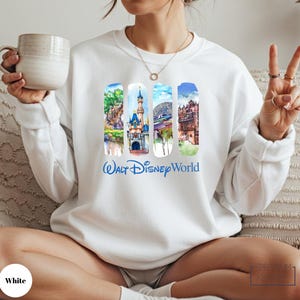 A woman wearing a white sweater with a collage of Disney World images and the text " Walt Disney World" printed on it, holding a mug and making a peace sign.