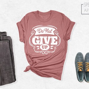 May include: A dusty rose t-shirt with a white graphic that says "Do Not Give Up" in a vintage style font.