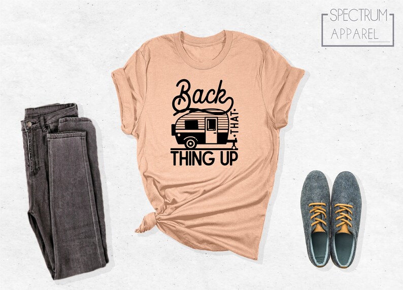 Może przedstawiać: R&oacute;żowy t-shirt z czarnym nadrukiem przedstawiającym przyczepę kempingową i tekstem "Back that thing up".