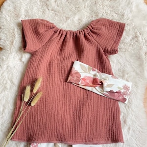 Könnte beinhalten: Ein rostfarbenes, schulterfreies, kurzärmeliges Kleid mit gerafftem Ausschnitt. Das Kleid wird mit weißen Leggings mit einem floralen Muster in Rosa- und Brauntönen kombiniert.