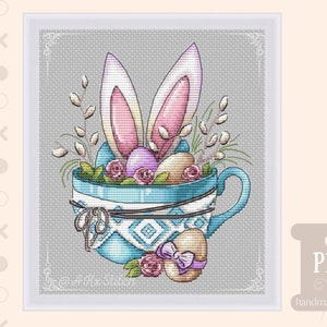 May include: A blue teacup with a white and blue geometric pattern is filled with Easter eggs, bunny ears, and spring flowers. The teacup has a handle and is decorated with a brown ribbon.