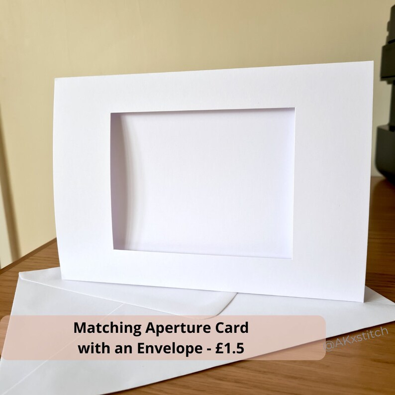 May include: White card with a rectangular aperture in the center. The card is on top of a white envelope. The text "Matching Aperture Card with an Envelope - &pound;1.5" is printed on the envelope.