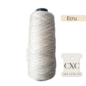 Könnte beinhalten: Eine Spule ecru-farbener Garn mit einem Etikett mit der Aufschrift "CXC ANY LENGTH".