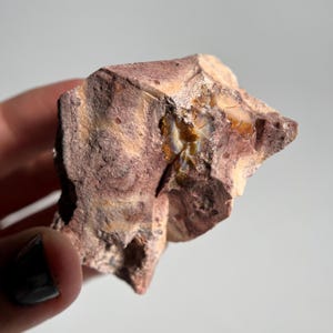 May include: A rough-hewn stone with a mix of colors, including reddish-brown and beige. The stone has a layered appearance with a section of iridescent, golden-hued material. The overall texture is coarse and natural, suggesting a raw mineral specimen.