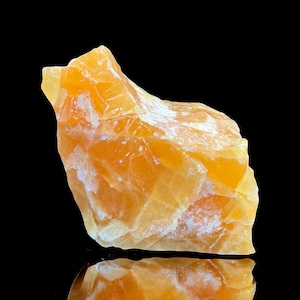May include: A large, rough, orange calcite crystal with a white, cloudy texture. The crystal is sitting on a black surface.