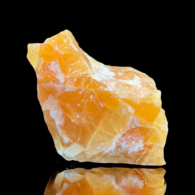 May include: A large, rough, orange calcite crystal with a white, cloudy texture. The crystal is sitting on a black surface.