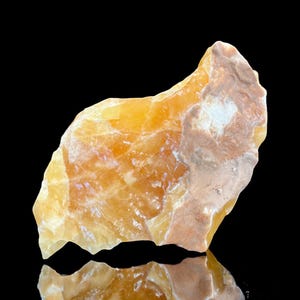 May include: A large, rough, orange-brown calcite crystal with a smooth, polished surface. The crystal has a natural, raw look and is a beautiful example of this mineral.